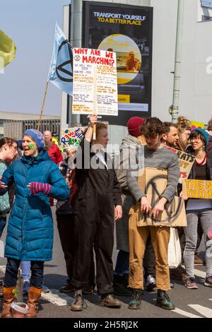 Straßenfoto einer Gruppe von Demonstranten des Klimawandels mit verschiedenen Plakaten. Straßenschild hinter „Transport yourself to a better place“. Stockfoto