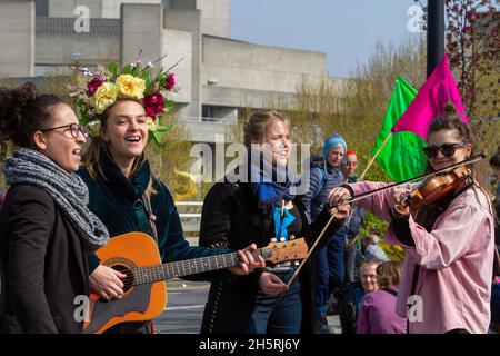 Straßenfoto einer Gruppe junger Demonstranten mit Instrumenten, die bei einer Demonstration zum Klimawandel spielen. Flaggen und Mitglieder der Öffentlichkeit dahinter. Stockfoto