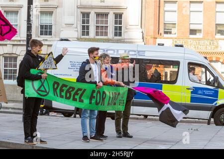 Straßenfoto einer Gruppe von Demonstranten mit großen grünen Rebellen für Leben Banner und Fahnen. Im Hintergrund ist ein Polizeifahrzeug geparkt. Stockfoto