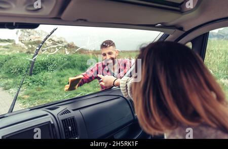 Mann putzt die Windschutzscheibe des Transporters, während die Frau auf den Fleck zeigt Stockfoto