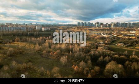 Flug über Stadtblöcke. Es gibt einen Park in der Nähe. Fliegen im Hintergrund der untergehenden Sonne. Luftaufnahmen. Stockfoto