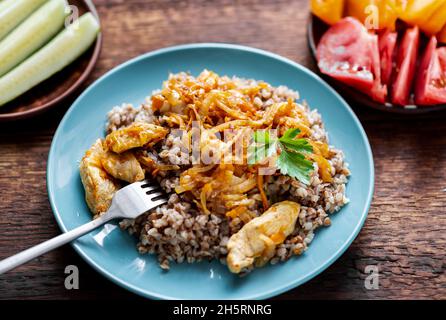 Buchweizenbrei mit Fleisch, Zwiebeln und Karotten auf Holzgrund. Mit frischem Gemüse, Gurken und Tomaten. Stockfoto