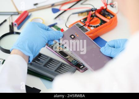 Meister öffnet die hintere Abdeckung des Mobiltelefons in der Nähe der Werkstatt Stockfoto