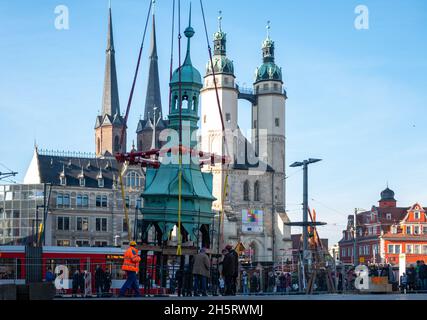 11. November 2021, Sachsen-Anhalt, Halle (Saale): Die Turmspitze des Stadthauses in Halle/Saale schwebt vom Gebäude auf den Kranhaken vor den Türmen der Stadtkirche auf den Markt. Das historische Stadthaus wird derzeit renoviert. Im Zuge der Arbeiten am Dachstuhl und an der Stuckdecke im Bankettsaal wurde nun auch der mit Kupferfolie verkleidete schiefe Turmhelm demontiert. Während der Arbeiten am Gebäude wird der Turm im Innenhof des Stadthauses stehen. Das neogotische Neorenaissance-Tagungs- und Festgebäude wurde 1894 eingeweiht. Im Jahr 19 Stockfoto