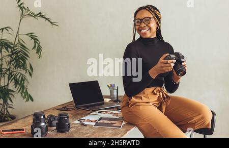 Fotografie macht mich glücklich. Kreative Freiberuflerin lächelt fröhlich, während sie eine dslr-Kamera in ihrem Heimbüro hält. Junge künstlerische Fotografin Stockfoto