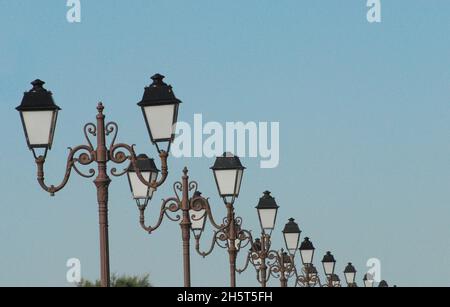 Nahaufnahme einer langen Reihe von prunkvollen Straßenlaternen in schwindender Perspektive. Gedreht in Saintes-Marie-de-la-Mer, Frankreich. Stockfoto