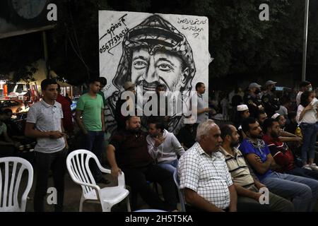 Palästinenser in der Nähe eines Wandbildes, das den verstorbenen palästinensischen Führer Yasser Arafat am 11. November 2021 in Rafah im südlichen Gazastreifen zeigt. Stockfoto