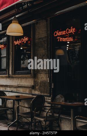 Außen und Veranda eines gemütlichen türkischen Cafés mit braunen Holztischen und -Stühlen und roten Neonschildern. Straßenstil. Stockfoto