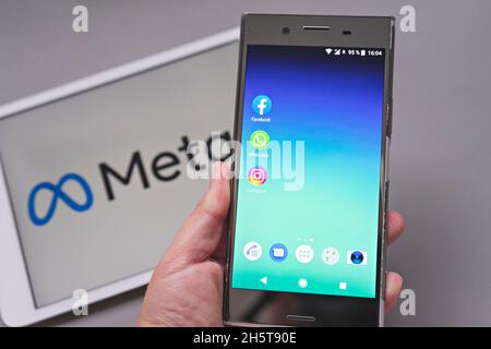 Mobiles Display mit Logo der Facebook-, WhatsApp- und Instagram-Apps vor verschwommenem META-Logo auf weißem Hintergrund Stockfoto