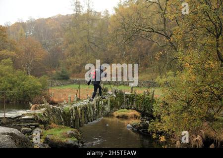 Walker überquert die Slater-Brücke in Little Langdale, im Lake District Nationalpark, Cumbria, England, Großbritannien. Stockfoto