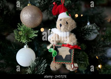 Teddybär hält an der Hoffnung fest, mit Glitzerkugeln, die am Weihnachtsbaum hängen Stockfoto