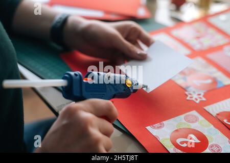 Nahaufnahme einer unerkennbaren jungen Frau, die Briefumschläge mit Geschenken für Kinder an Bord klebt, um den Weihnachtsadventkalender zu Hause zu gestalten. Stockfoto