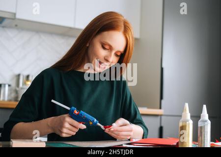 Nahaufnahme einer lächelnden jungen Frau, die Briefumschläge mit Geschenken für Kinder an Bord klebt, um den Weihnachtsadventkalender zu Hause zu gestalten. P Stockfoto