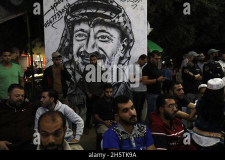 Palästinenser in der Nähe eines Wandbildes, das den verstorbenen palästinensischen Führer Yasser Arafat am 11. November 2021 in Rafah im südlichen Gazastreifen zeigt. Stockfoto