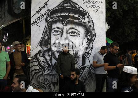 Palästinenser in der Nähe eines Wandbildes, das den verstorbenen palästinensischen Führer Yasser Arafat am 11. November 2021 in Rafah im südlichen Gazastreifen zeigt. Stockfoto