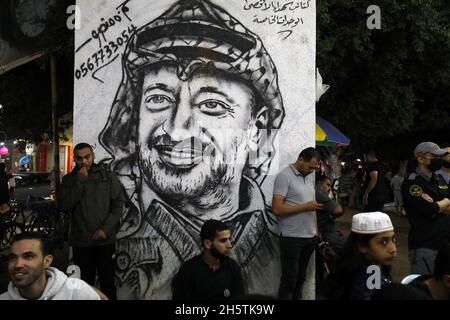 Palästinenser in der Nähe eines Wandbildes, das den verstorbenen palästinensischen Führer Yasser Arafat am 11. November 2021 in Rafah im südlichen Gazastreifen zeigt. Stockfoto