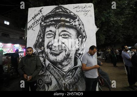 Palästinenser in der Nähe eines Wandbildes, das den verstorbenen palästinensischen Führer Yasser Arafat am 11. November 2021 in Rafah im südlichen Gazastreifen zeigt. Stockfoto