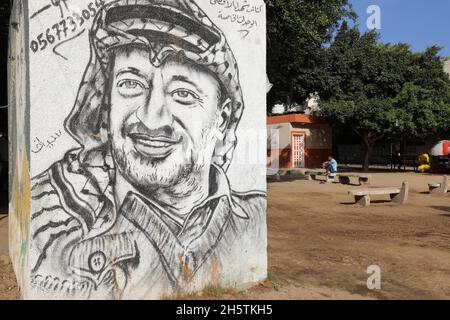Palästinenser in der Nähe eines Wandbildes, das den verstorbenen palästinensischen Führer Yasser Arafat am 11. November 2021 in Rafah im südlichen Gazastreifen zeigt. Stockfoto