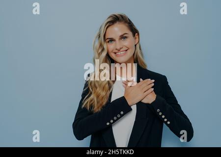 Fröhliches blondes Mädchen, das ihre Wertschätzung und Dankbarkeit zeigt, indem es die Hände auf die Brust legt Stockfoto