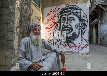 Palästinenser in der Nähe eines Wandbildes, das den verstorbenen palästinensischen Führer Yasser Arafat am 11. November 2021 in Rafah im südlichen Gazastreifen zeigt. Stockfoto