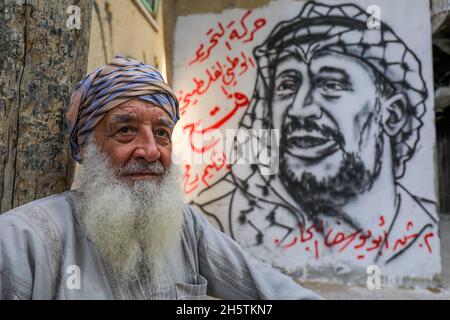 Palästinenser in der Nähe eines Wandbildes, das den verstorbenen palästinensischen Führer Yasser Arafat am 11. November 2021 in Rafah im südlichen Gazastreifen zeigt. Stockfoto