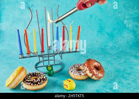 Happy Hanukkah und Hanukkah Sameach - traditioneller jüdischer Kerzenständer mit Kerzen, Donuts und Spinning Tops auf blauem Hintergrund. Stockfoto