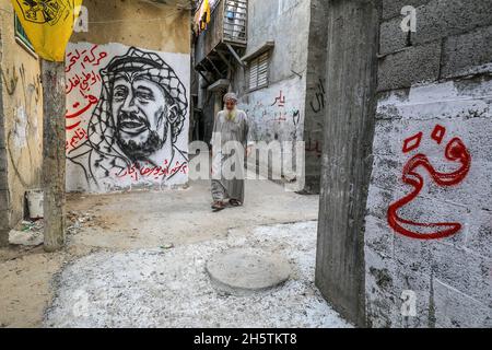 Palästinenser in der Nähe eines Wandbildes, das den verstorbenen palästinensischen Führer Yasser Arafat am 11. November 2021 in Rafah im südlichen Gazastreifen zeigt. Stockfoto
