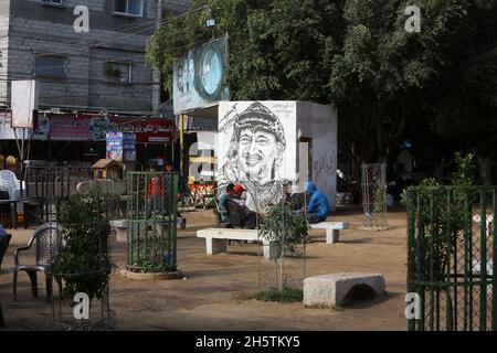 Palästinenser in der Nähe eines Wandbildes, das den verstorbenen palästinensischen Führer Yasser Arafat am 11. November 2021 in Rafah im südlichen Gazastreifen zeigt. Stockfoto