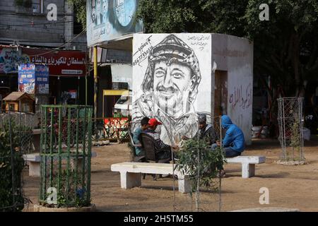 Palästinenser in der Nähe eines Wandbildes, das den verstorbenen palästinensischen Führer Yasser Arafat am 11. November 2021 in Rafah im südlichen Gazastreifen zeigt. Stockfoto