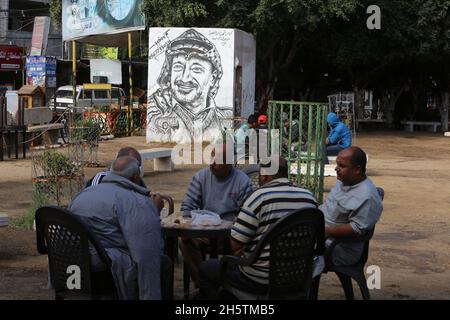 Palästinenser in der Nähe eines Wandbildes, das den verstorbenen palästinensischen Führer Yasser Arafat am 11. November 2021 in Rafah im südlichen Gazastreifen zeigt. Stockfoto