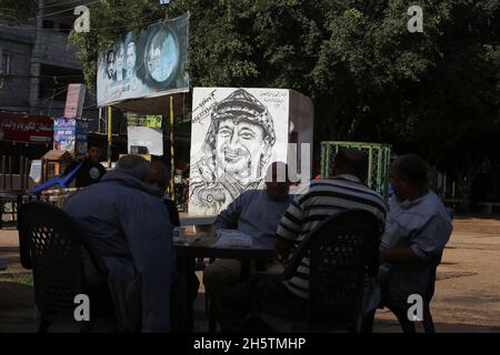 Palästinenser in der Nähe eines Wandbildes, das den verstorbenen palästinensischen Führer Yasser Arafat am 11. November 2021 in Rafah im südlichen Gazastreifen zeigt. Stockfoto
