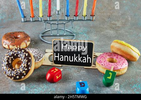 Happy Hanukkah und Hanukkah Sameach - traditioneller jüdischer Kerzenständer mit Kerzen, Donuts und Spinning Tops mit der Aufschrift Happy Hanukkah. Stockfoto