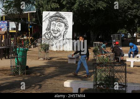 Palästinenser in der Nähe eines Wandbildes, das den verstorbenen palästinensischen Führer Yasser Arafat am 11. November 2021 in Rafah im südlichen Gazastreifen zeigt. Stockfoto