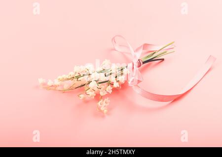 Maiglöckchen, gebunden mit einem rosa Band auf einem rosa Hintergrund. Zartes Federkonzept Stockfoto