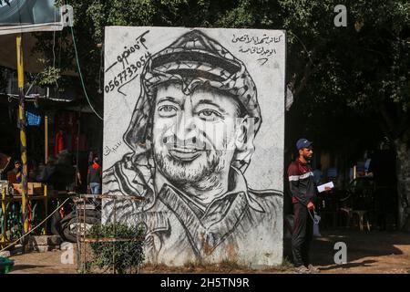 Palästinenser in der Nähe eines Wandbildes, das den verstorbenen palästinensischen Führer Yasser Arafat am 11. November 2021 in Rafah im südlichen Gazastreifen zeigt. Stockfoto
