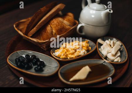 Traditionelles türkisches Frühstück mit Spiegelei, schwarzen Oliven, Croissant, Brot, Käse, Butter in Honig und Tee auf einem Holztisch. Bio, frisch und ta Stockfoto