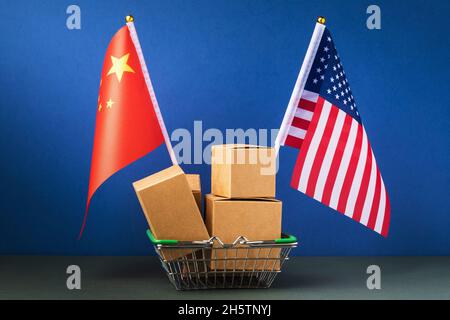 Verschiedene Boxen in einem Lebensmittelkorb und zwei Flaggen auf blauem Hintergrund, das Konzept des Handels zwischen China und den Vereinigten Staaten von Amerika Stockfoto