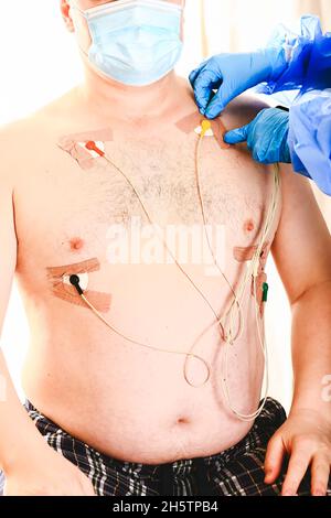 Der Arzt legt einen holter an die Brust des Mannes. Tägliche Überwachung des Herzens. Kardiologie. Stockfoto