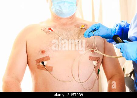 Der Arzt legt einen holter an die Brust des Mannes. Tägliche Überwachung des Herzens. Kardiologie. Stockfoto