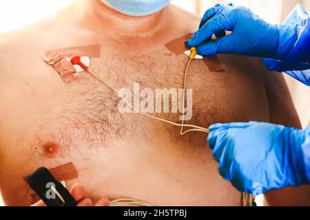 Der Arzt legt einen holter an die Brust des Mannes. Tägliche Überwachung des Herzens. Kardiologie. Stockfoto