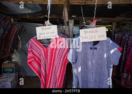 Farbenfrohe Bergsteiger-Shirts in Blau und Rot, die auf dem Regal hängen, mit einem Preisschild in thailändischer Sprache für ein ländliches Bekleidungsgeschäft. Stockfoto