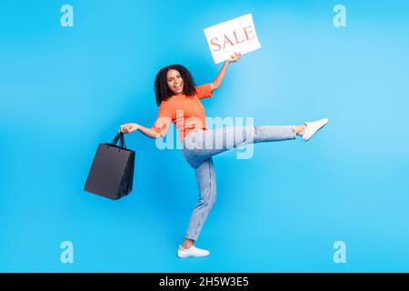 In voller Länge Profil Seite Foto von jungen afro Frau glücklich Lächeln halten Banner Verkauf Shop Tasche isoliert über blauen Hintergrund Stockfoto
