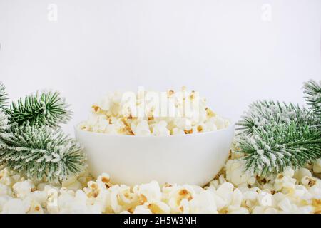 Popcorn in einer weißen Schüssel neben Fichtenzweigen, auf weißem Grund. Selektiver Fokus. Weihnachts- oder Neujahrskonzept. Maismahlzeiten. Stockfoto