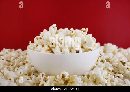 Popcorn in einer weißen Schüssel auf rotem Hintergrund. Selektiver Fokus. Mais-Snacks. Nahaufnahme. Stockfoto