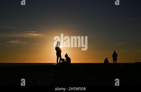 Brighton UK 11. November 2021 - Besucher versammeln sich am Brighton Strand bei Sonnenuntergang, um das tägliche Gemurmel der Stare zu beobachten. Die Stare versammeln sich jede Nacht in der Dämmerung zwischen November und März, bevor sie unter dem Pier roosting : Credit Simon Dack / Alamy Live News Stockfoto