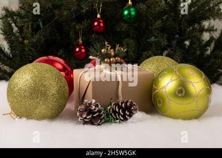 Weihnachts-Geschenkbox mit bunten Kugeln auf Kunstschnee, im Hintergrund ein Weihnachtsbaum mit hängenden Glühbirnen, Dekoration für den Urlaub dekoriert Stockfoto