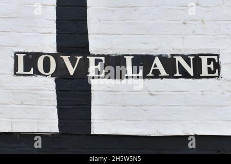 Nahaufnahme des Straßenschildes mit der Aufschrift „Love Lane“ auf einer schwarz-weiß gestrichenen Ziegelmauer in einer Stadt Stockfoto
