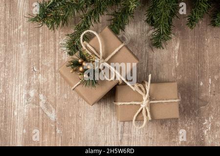 Detail der Geschenkschachteln in Papier mit Kordelbogen und einem kleinen Ornament eingewickelt, Hintergrund mit Holzstruktur und Baumzweig, Detail der Textur Stockfoto