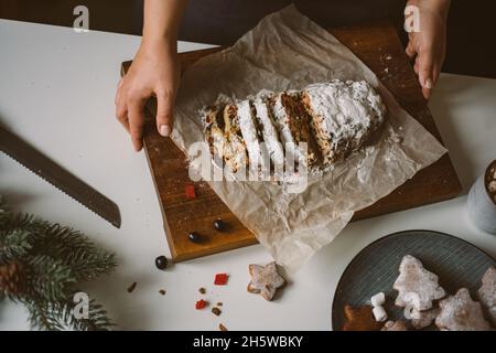 Die Frau serviert Weihnachtsgebäck, Stollen auf einem Holzbrett. Stimmungsvolles Foto der Vorbereitung auf die Feiertage, Draufsicht, selektiver Fokus Stockfoto