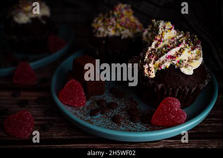 Leckere dunkle Schokolade Cupcake mit bunten Streuseln weißen Creme topin, Trüffel und herzförmigen Süßigkeiten für weihnachtsfeier für die Lieben Stockfoto